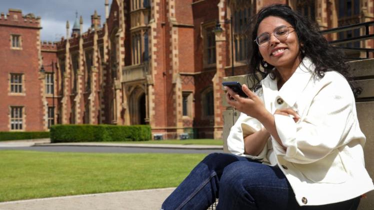 student sitting looking at phone in front of Queen's building